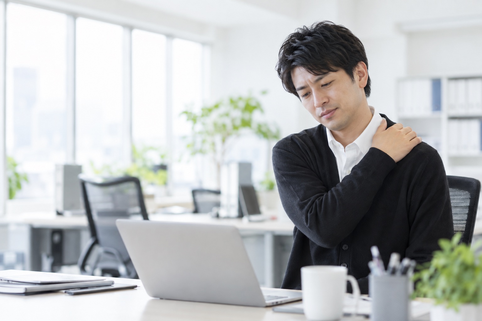 デスクワークで肩の疲れを感じる会社員のイメージ